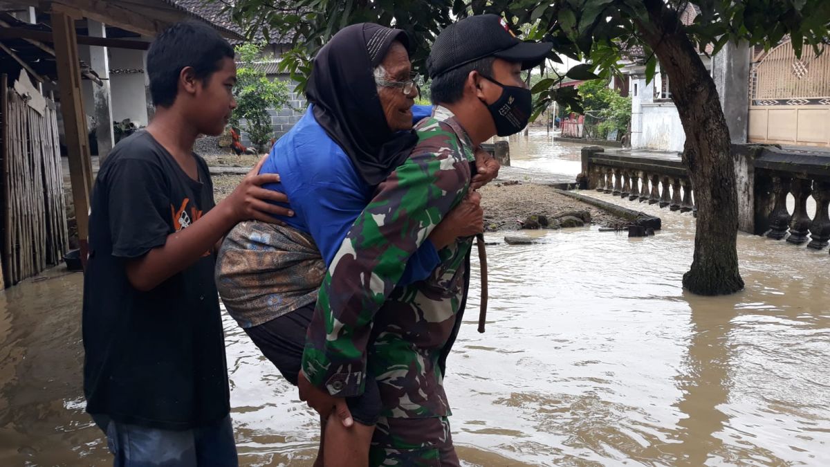 Personel TNI menggendong warga di tengah banjir akibat luapan Kali Lamong. (Foto: Sofan for jatimnow.com)