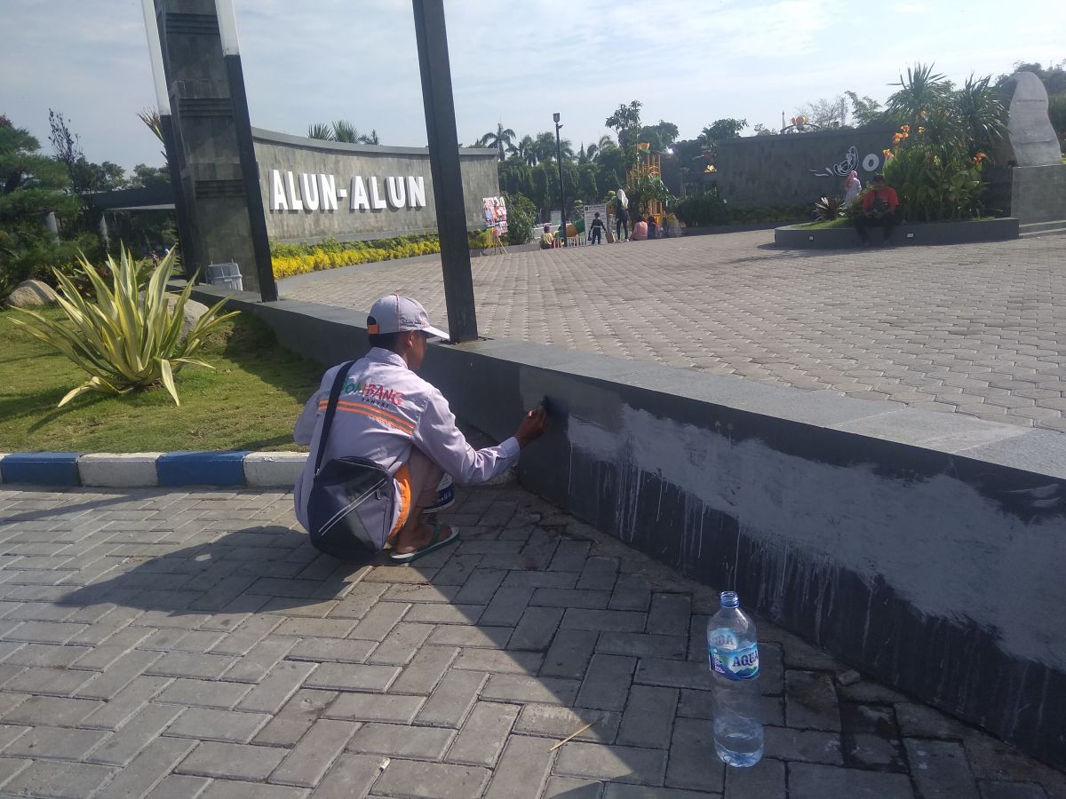 Petugas kebersihan dari DLH Jombang menghapus tulisan kalimat makian kepada polisi di pagar pembatas taman alun-alun Jombang.(Foto: Elok Aprianto/jatimnow.com)