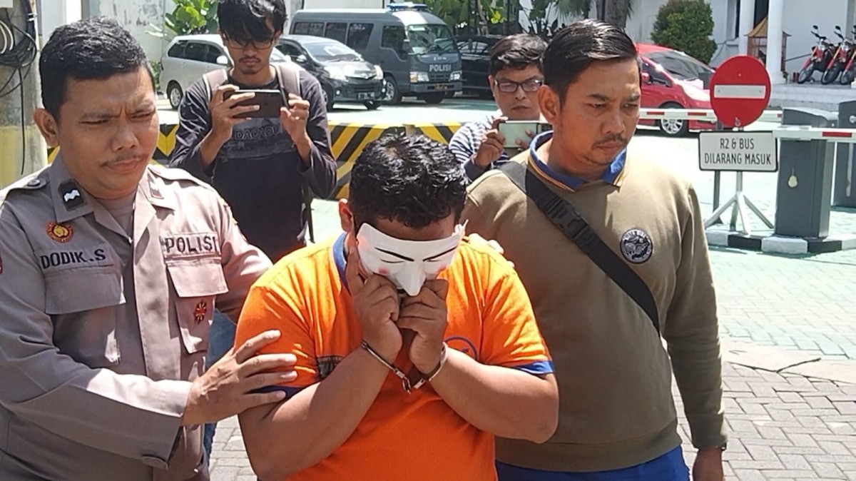 Guru cabul hanya bisa menutupi wajahnya setelah ditangkap Unit PPA Polrestabes Surabaya. (foto: Farizal tito/jatimnow.com)
