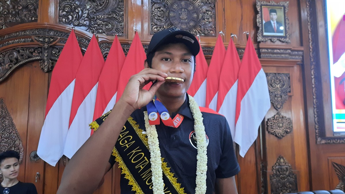 Bintang Akbar menggigit medali emas yang diraihnya di ajang voli pantai beregu putra Sea Games. (Achmad Supriyadi/jatimnow.com)