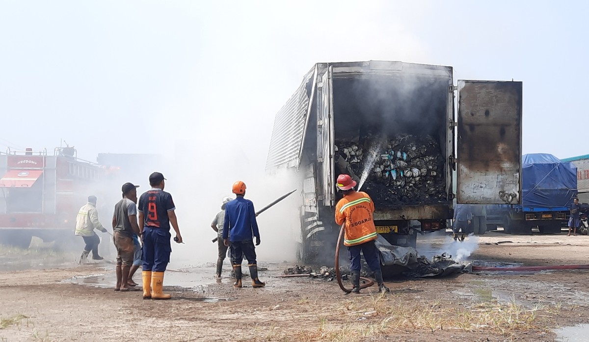 Petugas pemadam kebakaran saat menyemprotkan air ke muatan popok yang terbakar. (Foto: Achmad Supriyadi/jatimnow.com)
