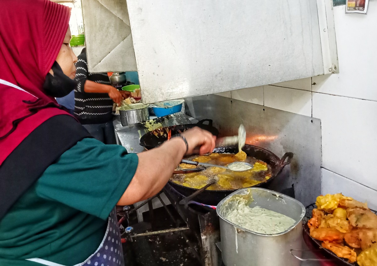 Ibu Istina berkerudung merah sedang menyiapkan gorengan untuk dibagikan. (Foto: Ahaddiini HM/jatimnow.com).