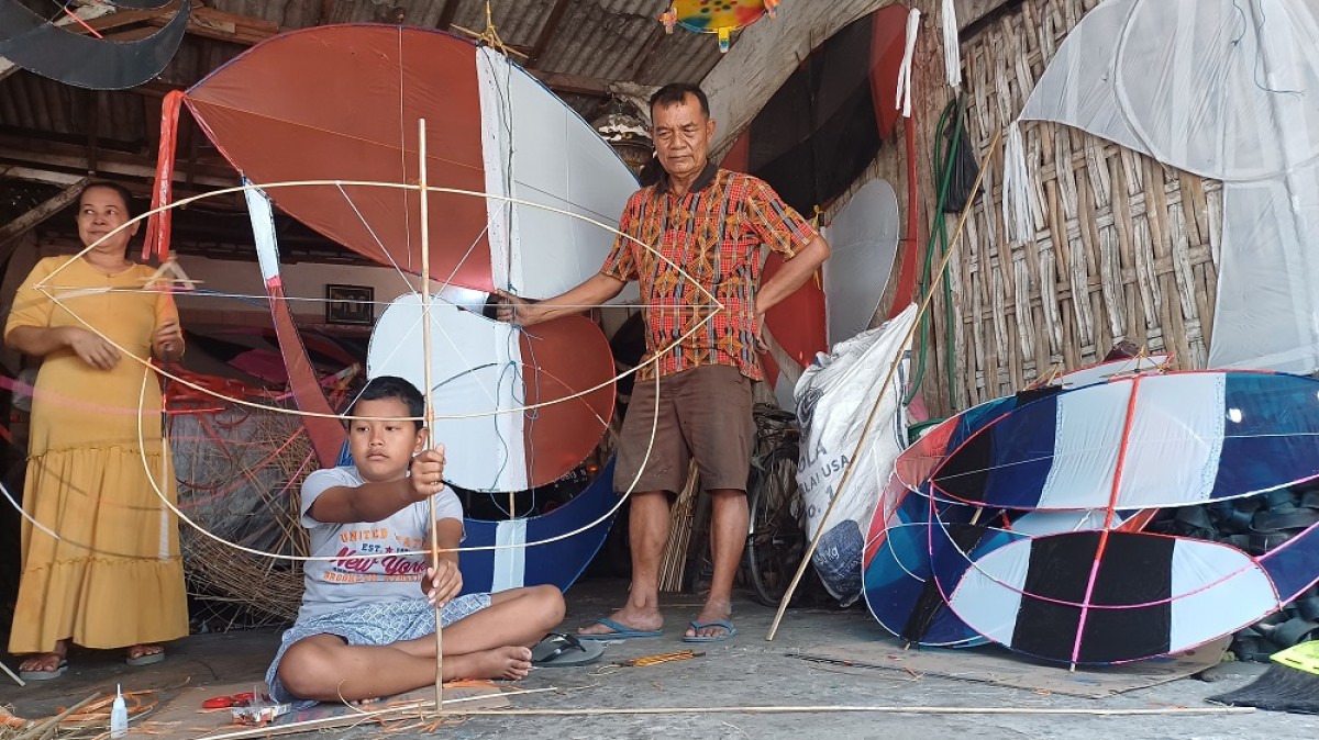Perajin layang-layang Lamongan, Jhony saat melakukan rutinitasnya bersama cucunya. (Foto: Adyad Ammy Iffansah/jatimnow.com)