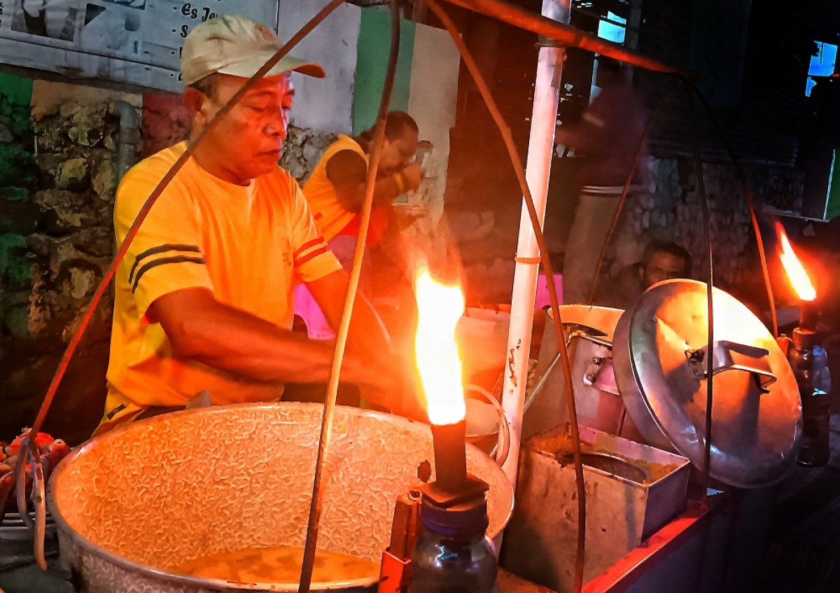 Sugito melayani pelanggan kuliner lontong cecek dan kupang. (Foto: Ahaddiini HM for jatimnow.com)