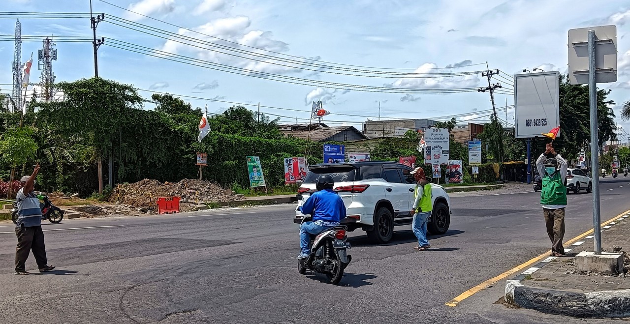 Agus Supriyanto (baju garis) dan Giyono (rompi hijau) saat menjalani rutinitas sebagai polisi cepek di bundaran Aloha Juanda Sidoarjo. (Foto: Ahaddiini HM/jatimnow.com)