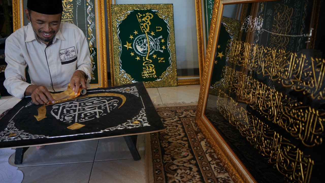 Komarudin saat menyelesaikan pesanan kaligrafi. (Foto: Bramanta Pamungkas/jatimnow.com)