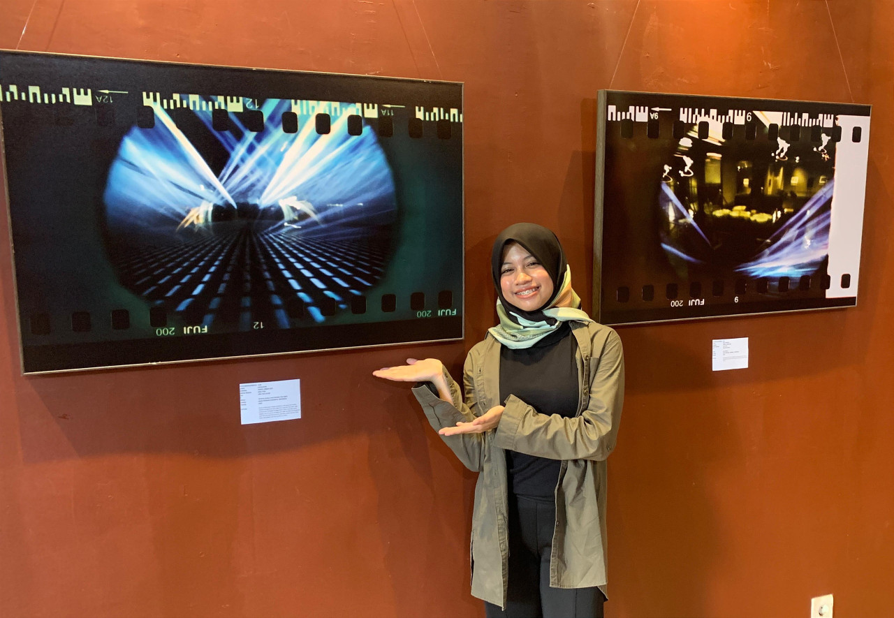 Alin di depan karya fotonya yang dibuat dengan kamera pinhole berjudul "Excalator" yang dipamerkan di Galeri Merah Putih Balai Pemuda Surabaya. (Foto: Sanggar Daun/jatimnow.com)