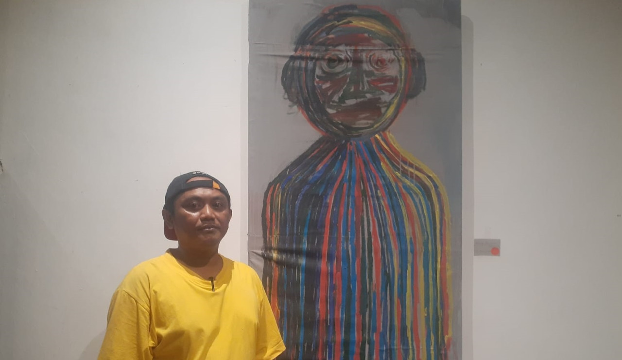 Bayu Kabo di samping karya lukisan berjudul Menuju Perjalanan Self Portrait. (Foto: Endang Pergiwati/jatimnow.com)