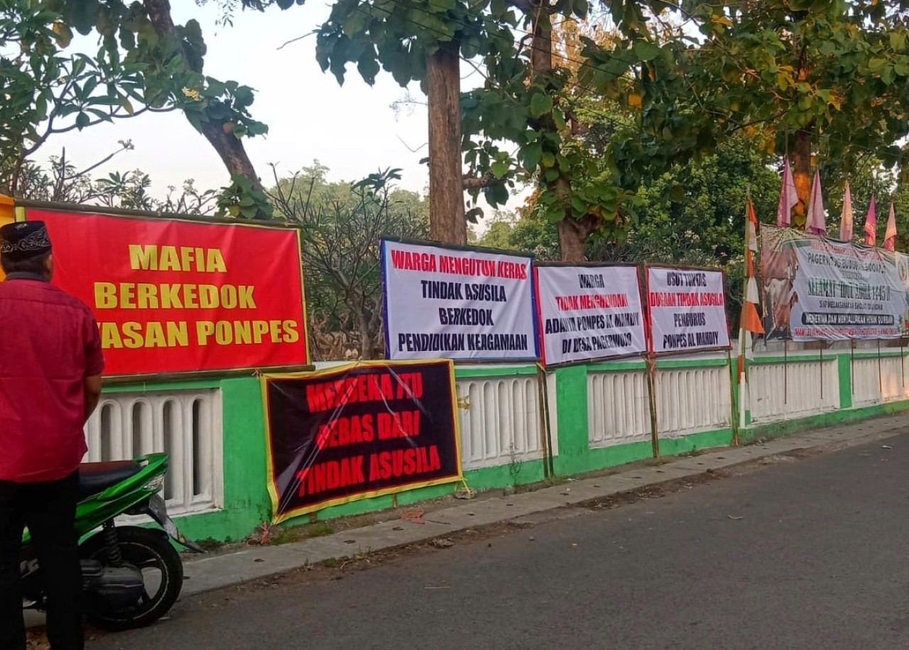 Banner dan poster berisi aksi protes ke pengurus ponpes Mahdy yang dipasang tepat didepan Pondok pesantren oleh warga Desa Pagerwojo Buduran Sidoarjo. (Foto: Ahaddiini HM/jatimnow.com).