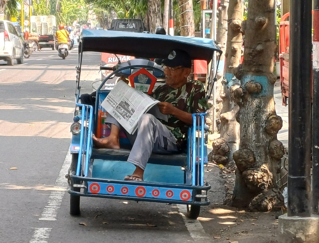 Ilustrasi. Potret tukang becak motor menyempatkan membaca surat kabar saat menunggu penumpang. (Foto: Adyad Ammy Iffansah/jatimnow.com)
