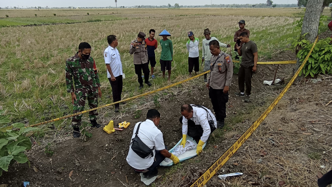 Polisi saat mengevakuasi jenazah bayi yang ditemukan tergeletak di area persawahan. (Foto: WhatsApp Grup/jatimnow.com)