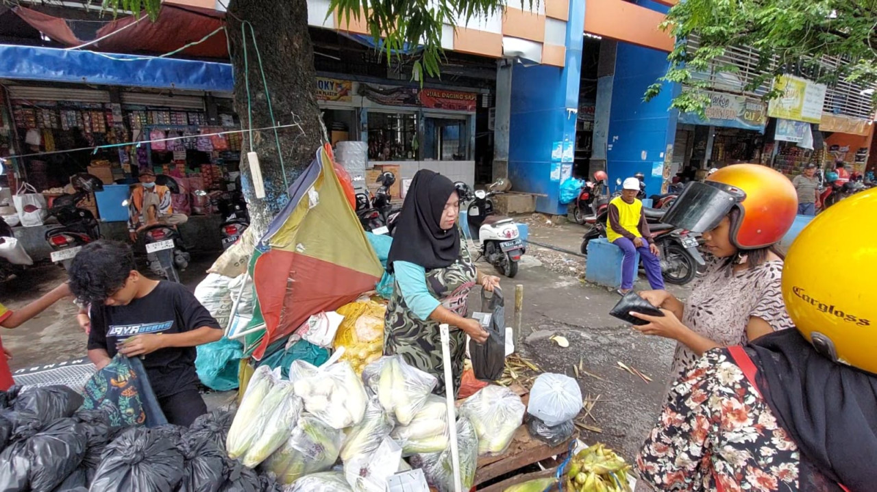 Vifa penjual jagung dan arang di Pasar Sidoharjo Lamongan saat melayani pembeli. (Foto : Adyad Ammy Iffansah/jatimnow.com)