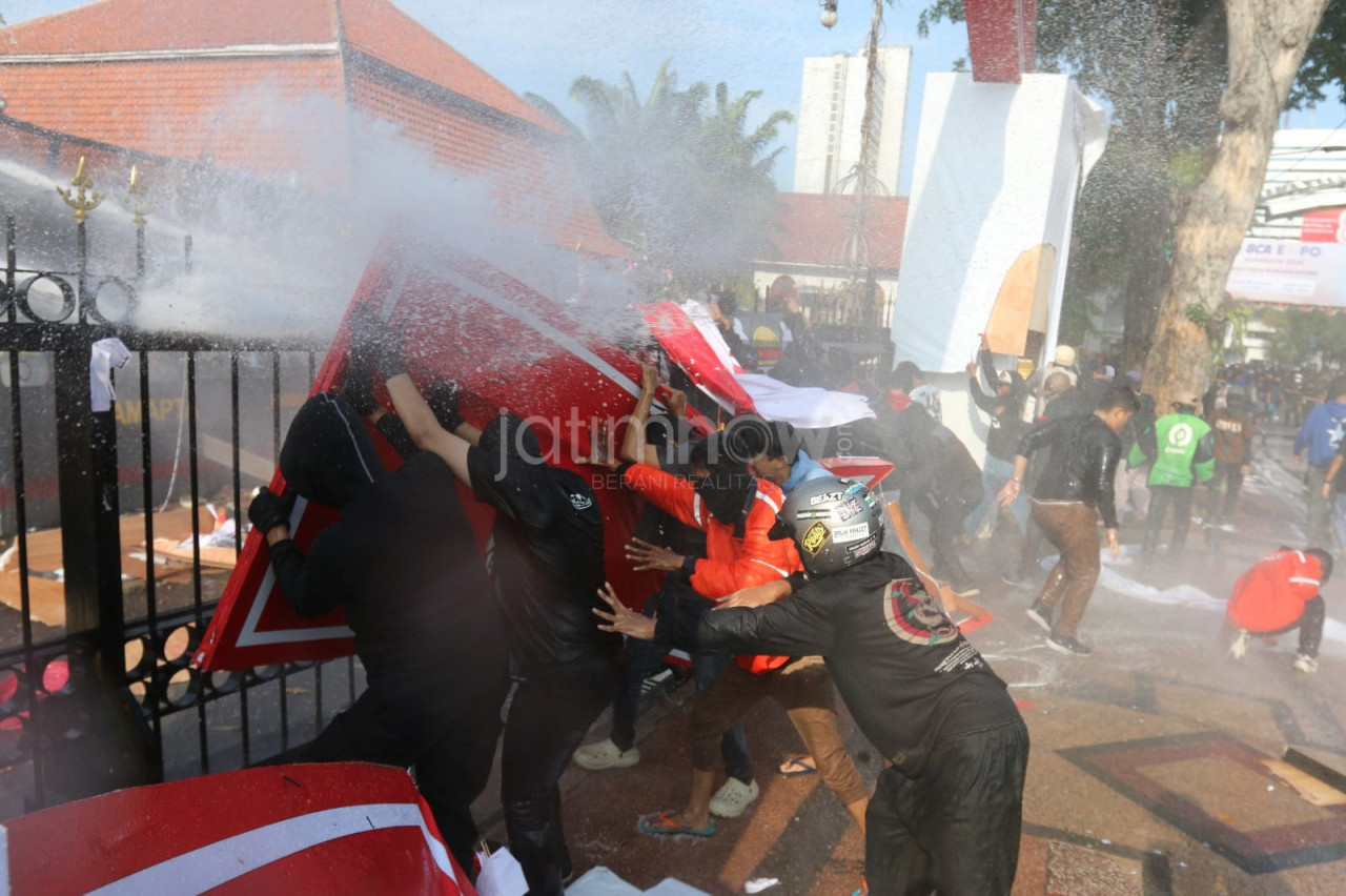 Foto: Massa berusaha menghindari semprotan water canon dari mobil polisi (Ridhoi for jatimnow.com)