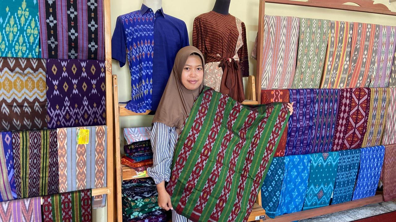 Yusna, penerus Siti Ruqoyah tengah memegang selembar kain tenun ikat Salur Tirto yang memikat di gerai Medali Mas 2. (Foto: Yanuar Dedy/jatimnow.com)