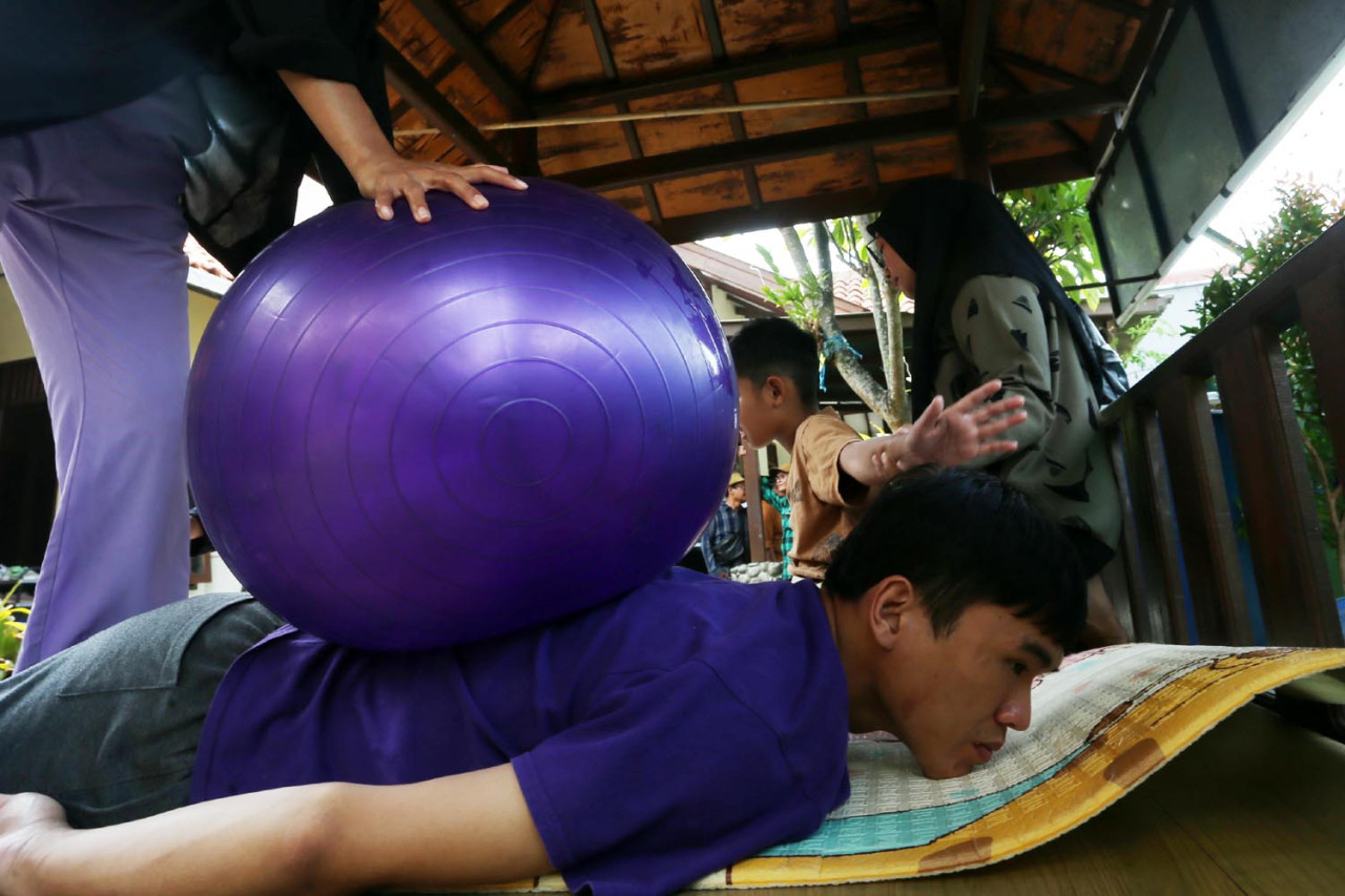 Seorang terapis di Malang Autism Center dengan sabar menekan bola terapi di punggung anak autisme untuk melatih sensorik dan relaksasi otot. (Foto: Ali Masduki/jatimnow.com)