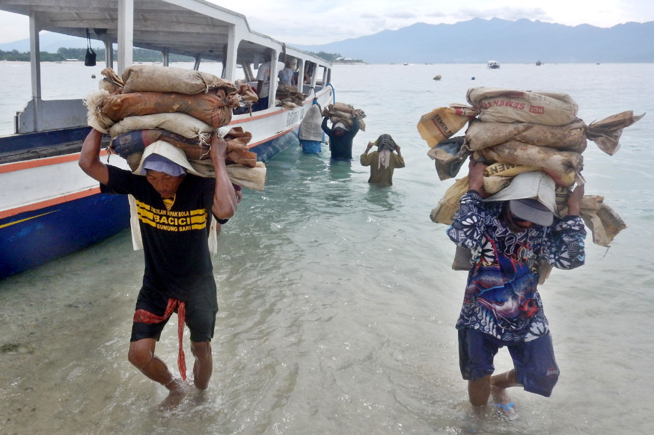 Kuli angkut memikul karung material bangunan dari perahu menuju daratan Gili Trawangan, Lombok, Jumat (26/12/2025). (Foto: Ali Masduki/jatimnow.com)