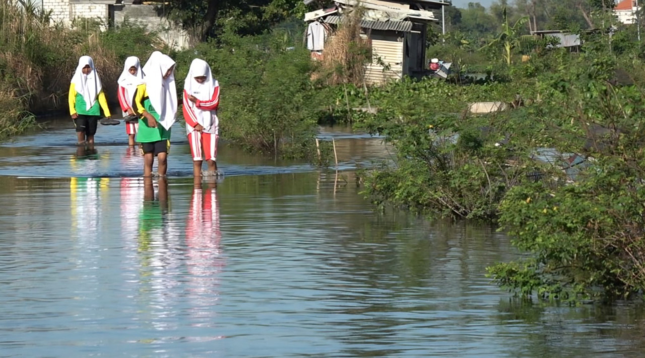 Foto: Para pelajar asal Desa Tejoasri, Kalitengah, Lamongan saat melewati genangan air banjir luapan bengawan jero. (Adyad Ammy Iffansah/jatimnow.com)