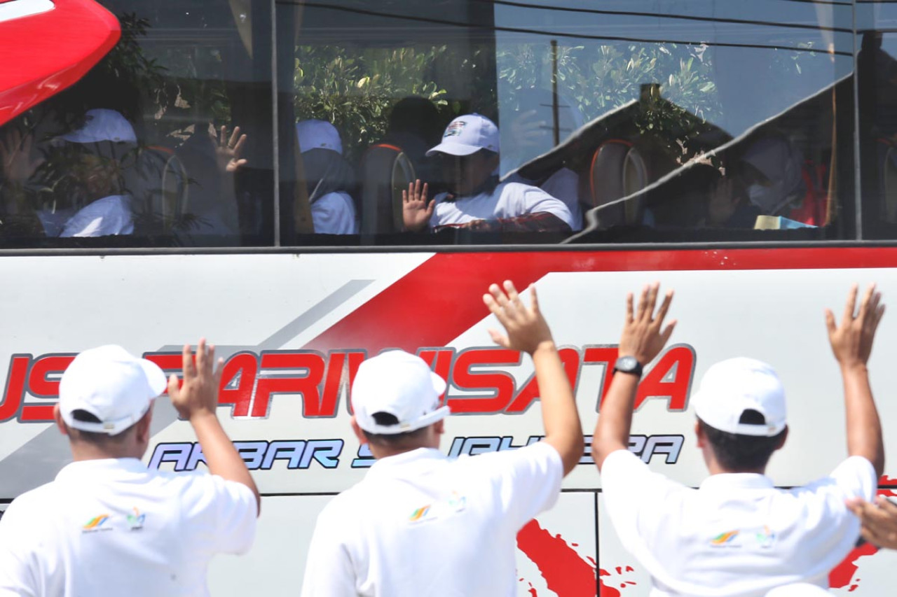Pemudik melambaikan tangan dari dalam bus saat pemberangkatan program mudik gratis PTPN I Regional 5 di Surabaya, Senin (17/3). Sebanyak 600 peserta diberangkatkan ke berbagai kota di Pulau Jawa. (Foto: Ali Masduki/jatimnow.com)
