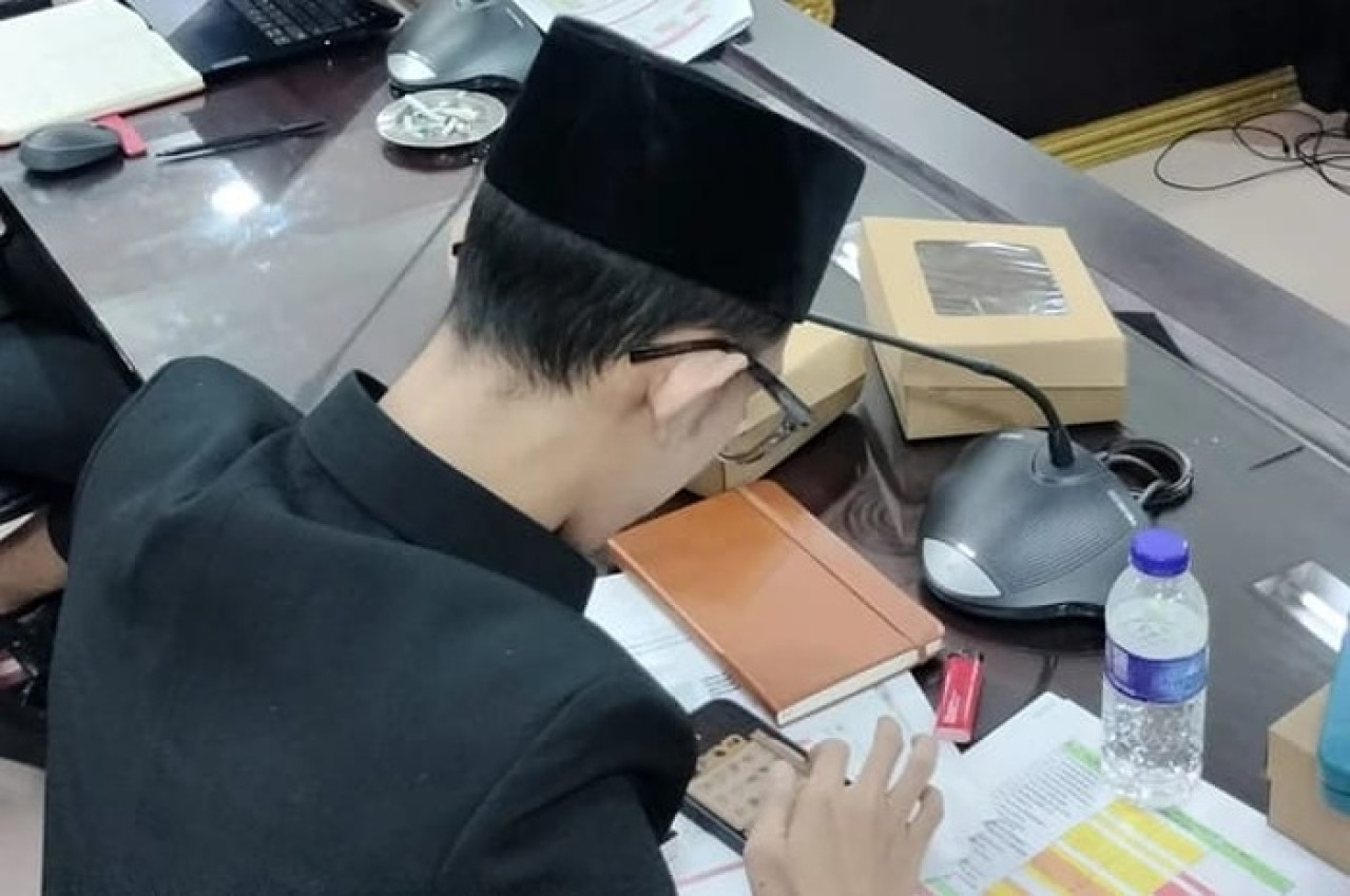 Lora Syahri saat bermain game dan merokok ketika rapat berlangsung. (Foto: Sutris/jatimnow.com)