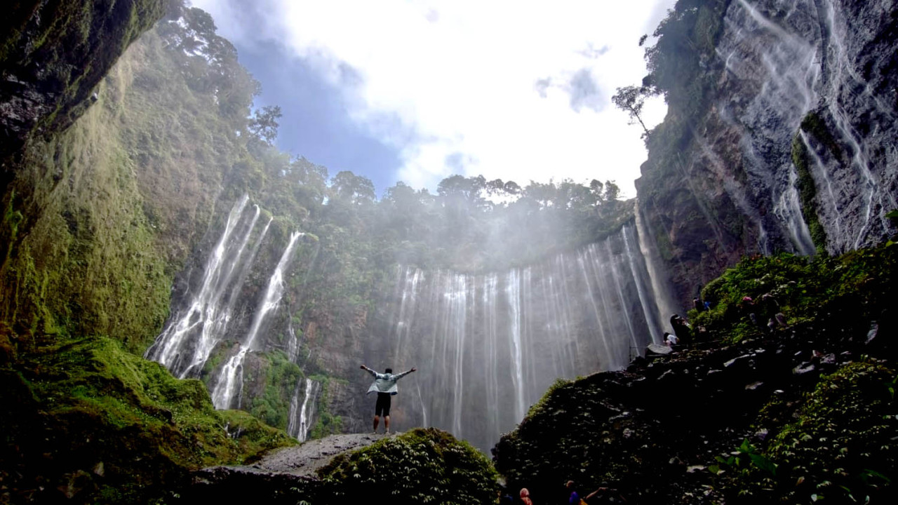 Seorang wisatawan berdiri menikmati keindahan Air Terjun Tumpak Sewu di Kabupaten Lumajang, Jawa Timur. Air terjun ini menjadi salah satu destinasi wisata alam unggulan di lereng Gunung Semeru. (Foto: Ali Masduki/jatimnow.com)