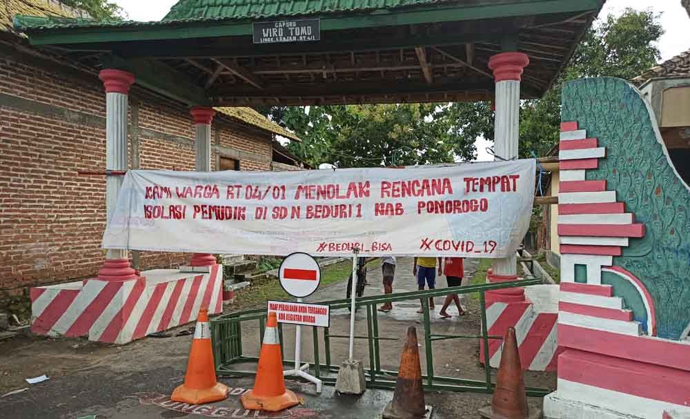 Warga menutup jalan menuju sekolah dasar yang akan dijadikan sebagai tempat isolasi pemudik