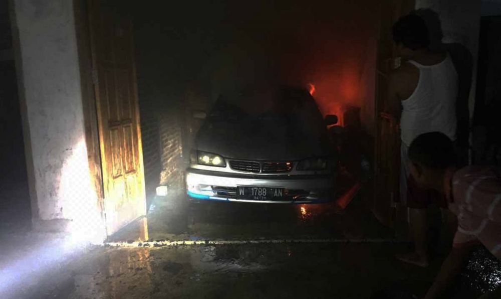 Pemilik dan warga berusaha memadamkan api yang membakar mobil