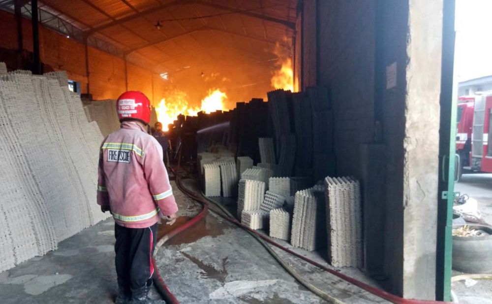 Petugas pemadam berusaha memadamkan api yang membakar pablik pembuatan egg tray di Blitar