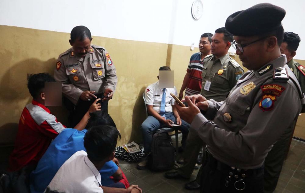 Anggota Satpol PP dan Polres Ponorogo memeriksa handphone milik 8 pelajar yang terjaring razia