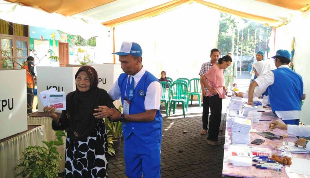 Petugas TPS di Pasuruan yang berseragam ala pelajar TK saat memandu pemilih manula
