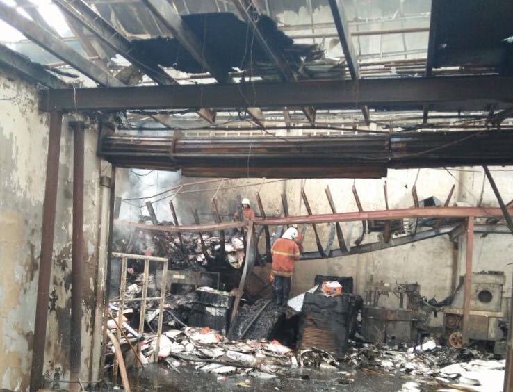 Petugas pemadam kebakaran melakukan pembasahan pada bangunan yang terbakar. 