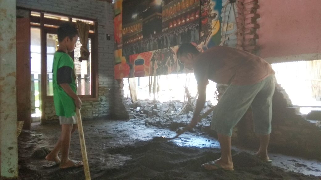 Korban banjir, Sulistiyo saat meratakan pasir lantai rumah yang jebol.