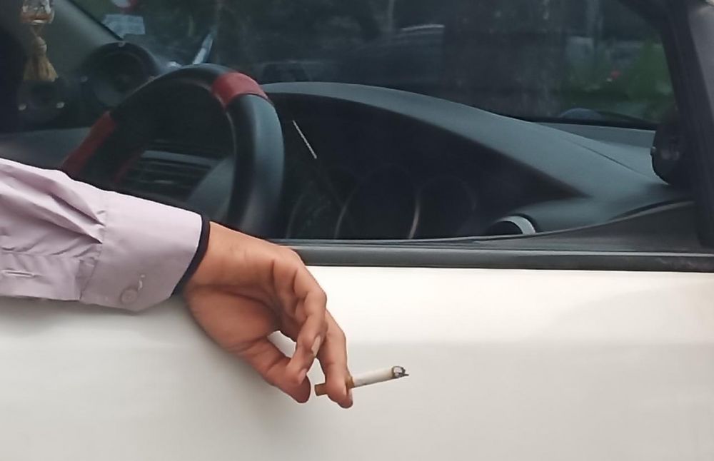 Pengemudi mobil merokok saat berhenti di lampu merah