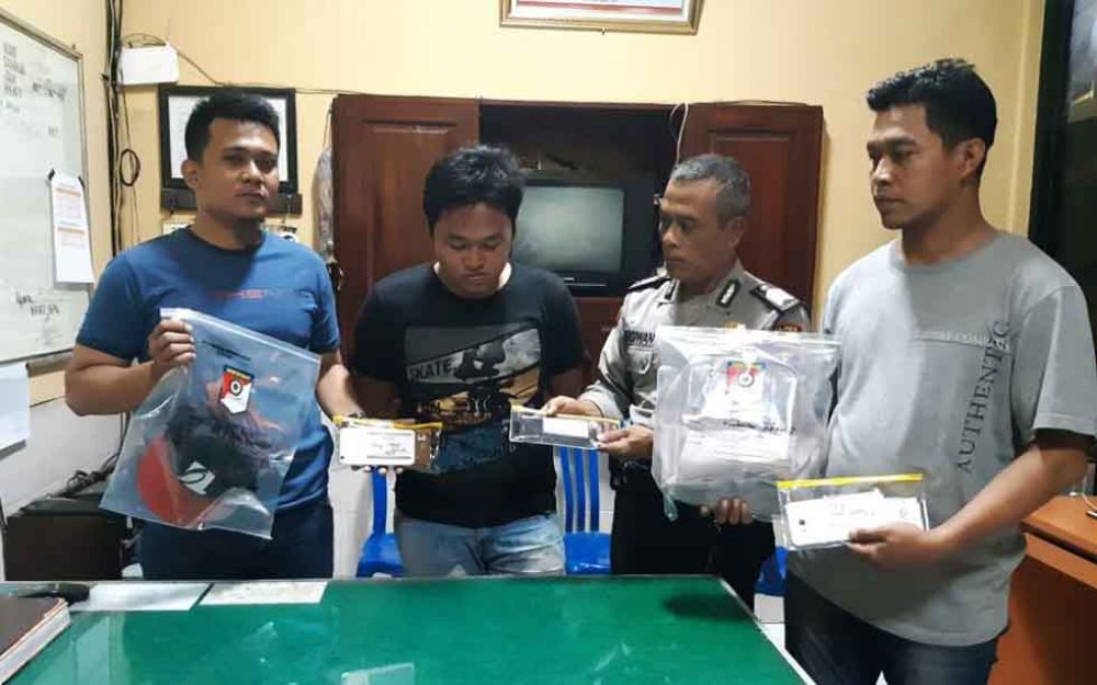 Tersangka (kaos hitam) bersama barang bukti saat di Mapolsek Ngoro